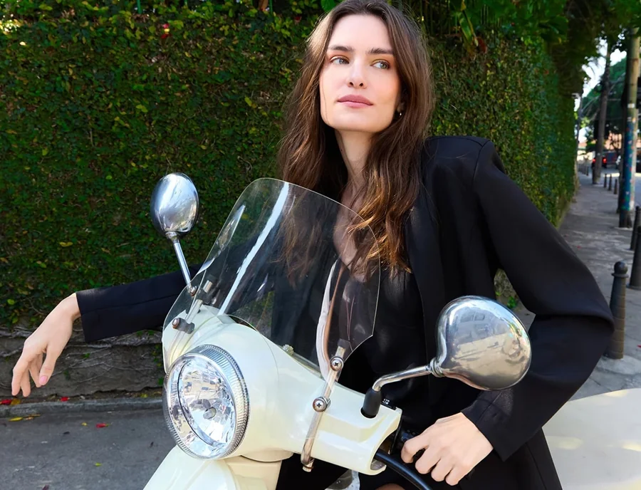 Model in a black blazer leaning on a vintage scooter